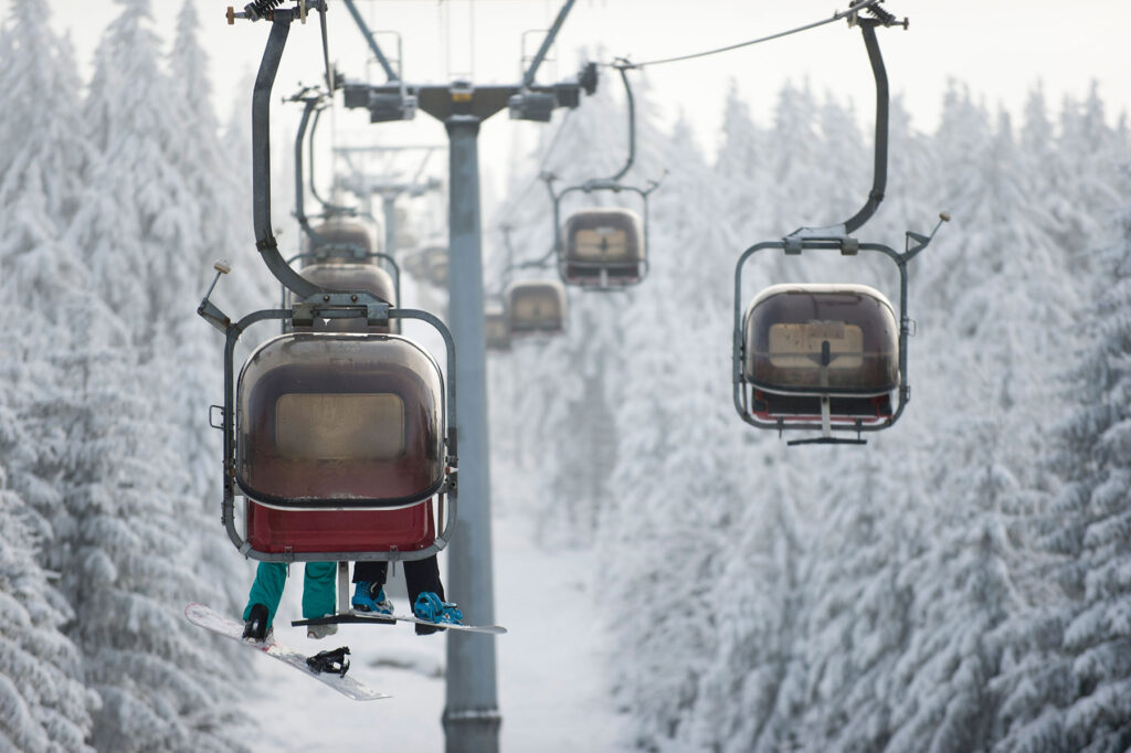 Ochsenkopf im Winter: Sesselbahn-Gondeln ziehen durch eine verschneite Waldlandschaft mit frostbedeckten Tannen, Winterszene am Hang.