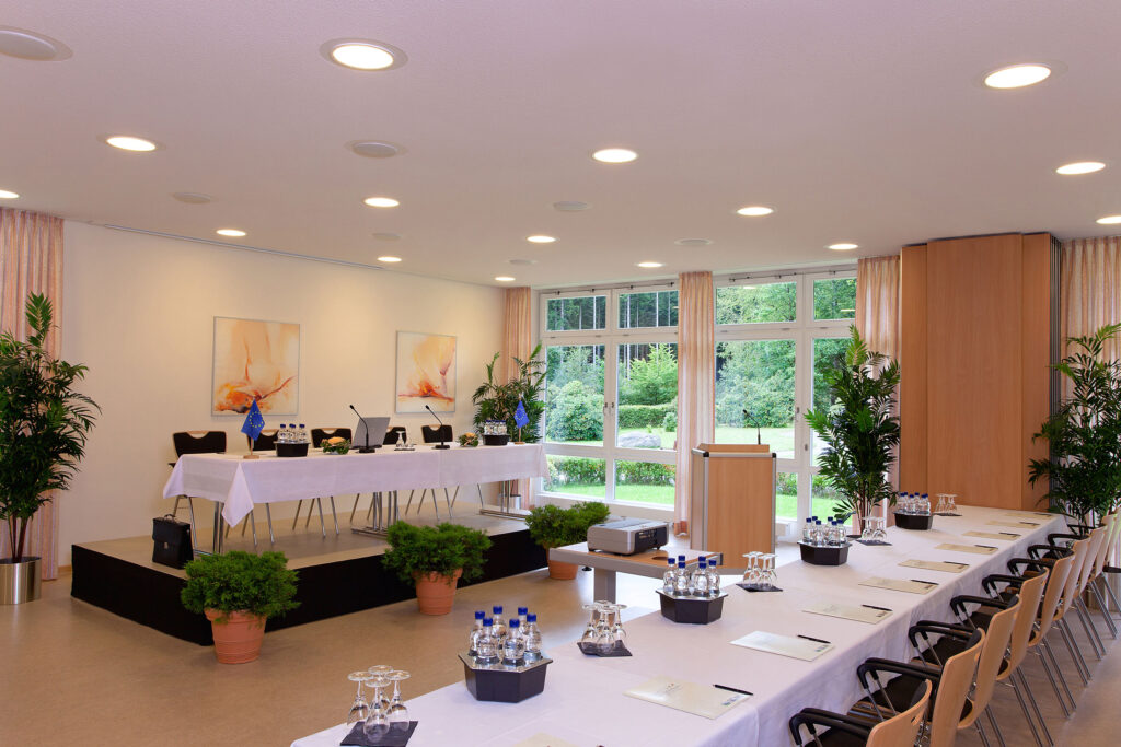 Konferenzraum im Hotel Haus Silberbach mit großer runder Tischanordnung, Dolmetscheranlage und moderner Tagungstechnik; Fensterfront mit Blick ins Grüne, Pflanzen und helle Beleuchtung