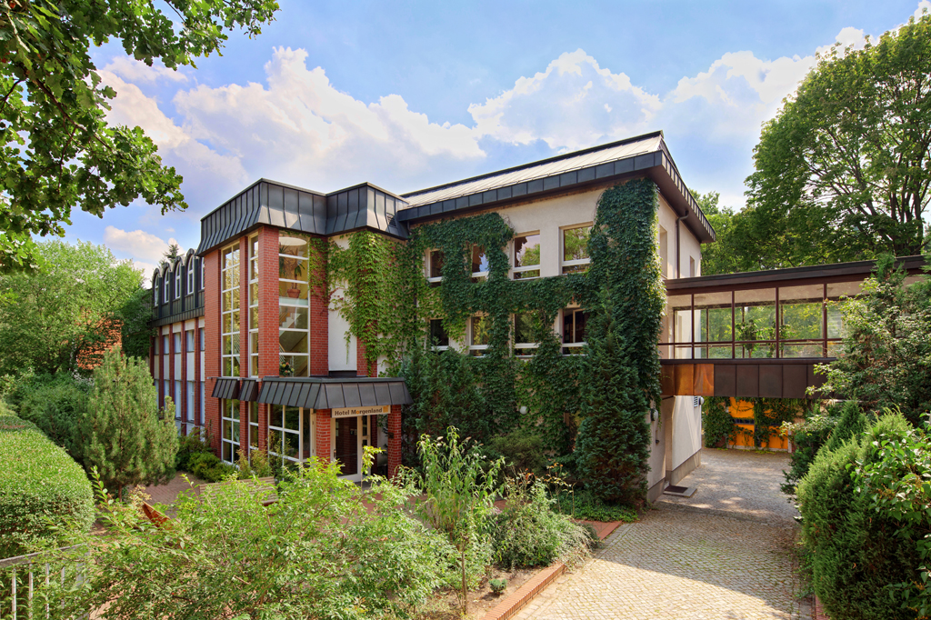 Das Hotel Morgenland zeigt sich als begrüntes Gebäude mit modernen Glasfassaden, gepflegtem Garten und überdachtem Eingangsbereich.